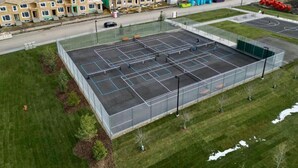 An aerial view of a sports court with multiple tennis courts, surrounded by a fence and greenery. - Modern Private Suite in a serene location 15 minutes away from the Airport. (Airdrie)