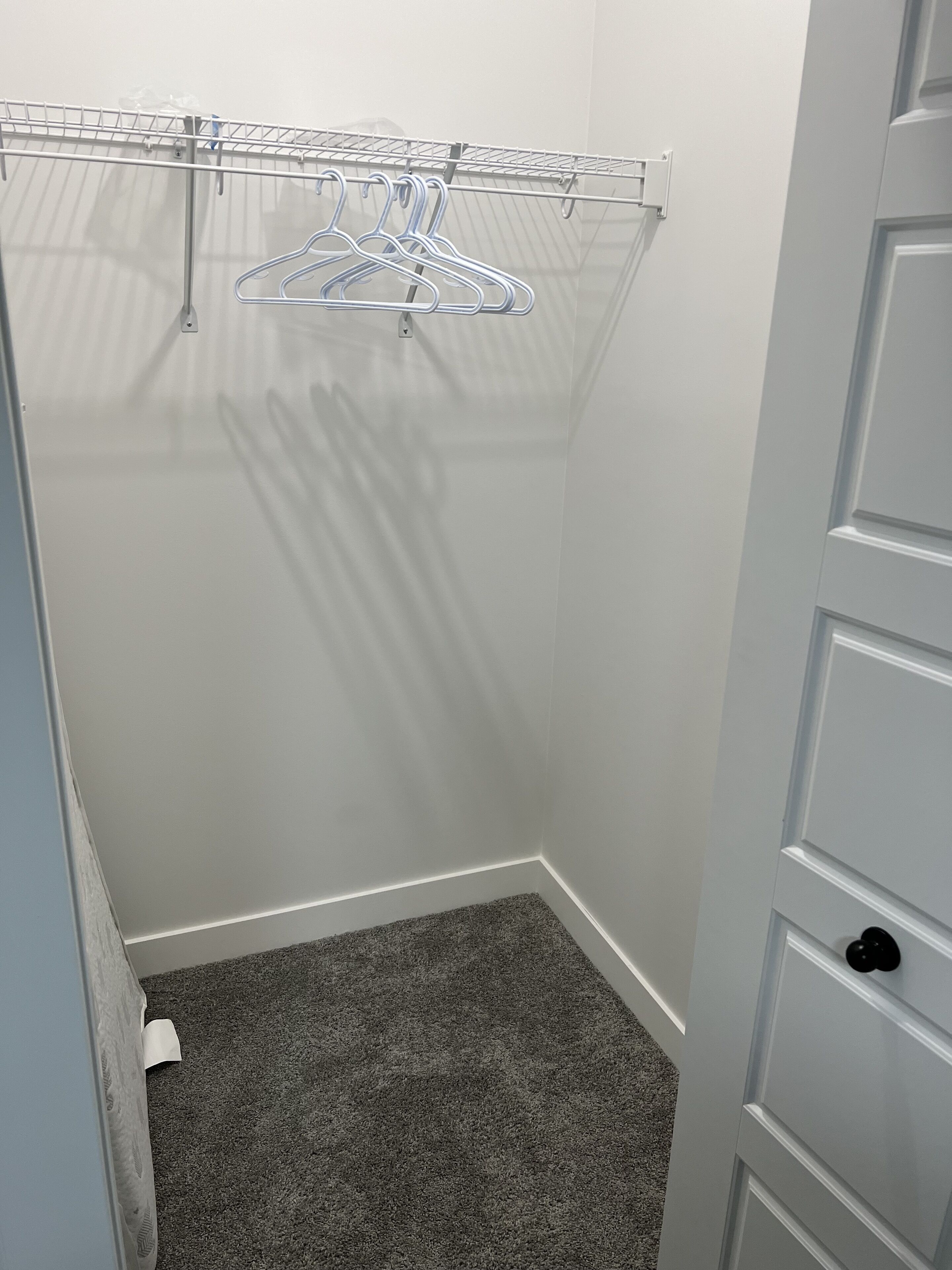 A small walk-in closet with a grey carpet, a metal drying rack, and a white door with a black handle.