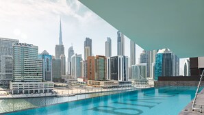 A cityscape with modern high-rise buildings, a prominent skyscraper, and a waterfront area with a pool. - LUX The Modern Binghatti Canal Suite (Dubai)