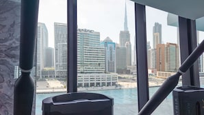 A view from a room with large windows overlooking a cityscape with modern buildings, including a prominent skyscraper. - LUX The Modern Binghatti Canal Suite (Dubai)