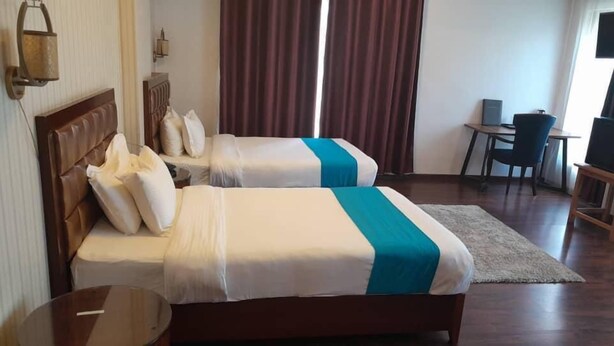 A hotel room with two beds, a desk, a chair, and a TV.