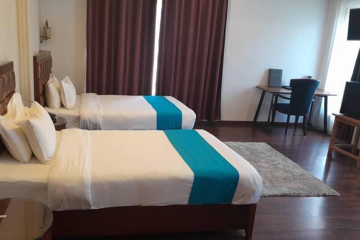 A hotel room with two beds, a desk, a chair, and a TV.