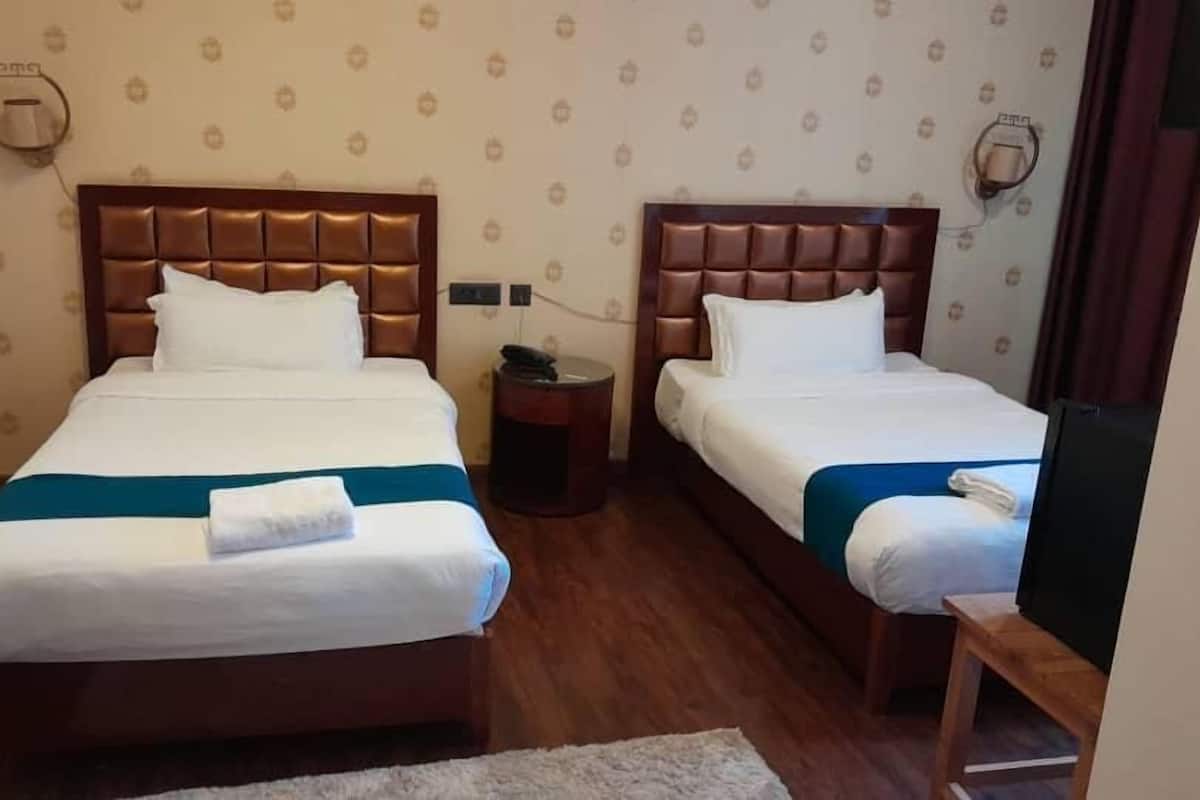 A hotel room with two beds, a small round table, a TV, and a patterned wall.