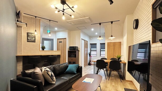A modern living room with a black leather sofa, a wooden dining table, and a flat-screen TV mounted on the wall. - Deep Osaka! A Running Lamp 2 minutes from the station! Ideal location for sightseeing in Namba & USJ Osaka! Up to 6 people are allowed at the same price (大阪市)