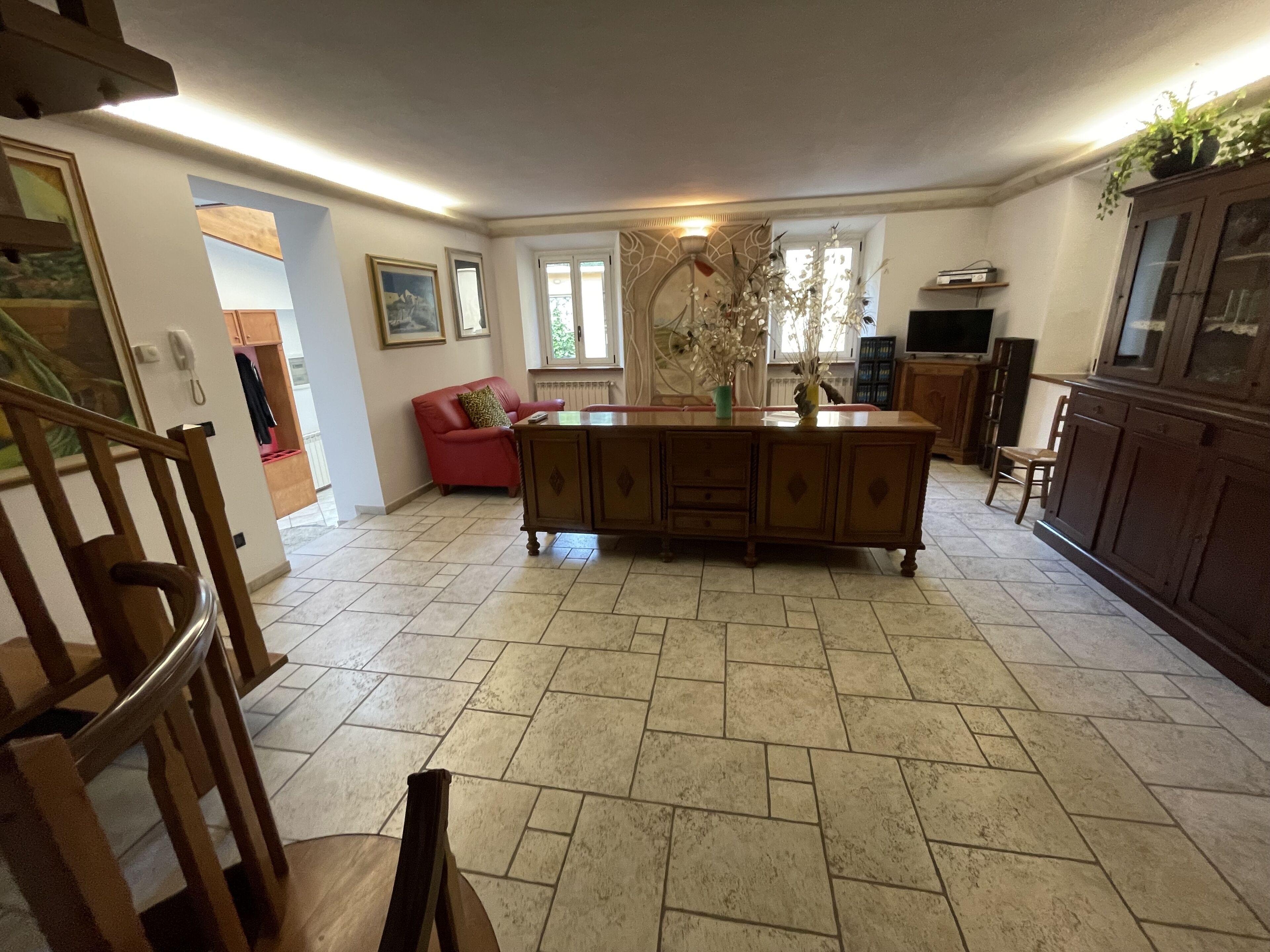 A spacious living area with a large wooden cabinet, a red sofa, and a dining table.