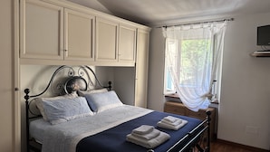 Een slaapkamer met een bed, een raam met gordijnen en een televisie aan de muur.