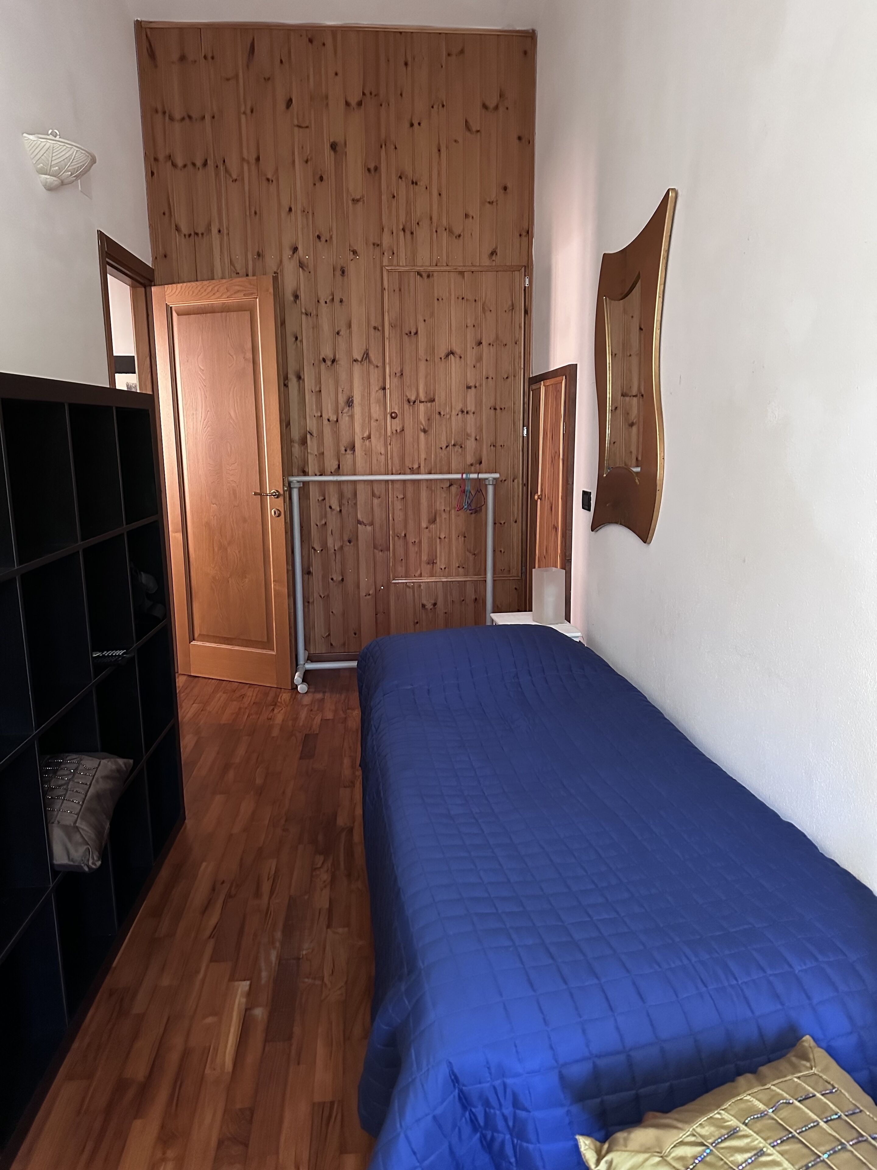 Quarto com guarda-roupa de madeira, cama com colcha azul e parede revestida em madeira.