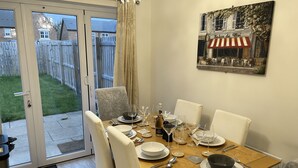 Comedor con una mesa dispuesta para seis personas, sillas, un cuadro y vistas a través de puertas de cristal.