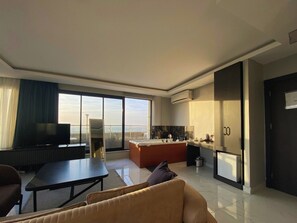 A modern living room with a sofa, a TV, a dining table, and a kitchen area with a refrigerator. - Elite Marmara Bosphorus Çamlıca (Istanbul)