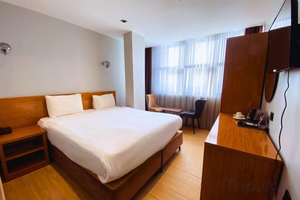A hotel room with a large bed, a desk with a chair, a television, and a window with curtains.