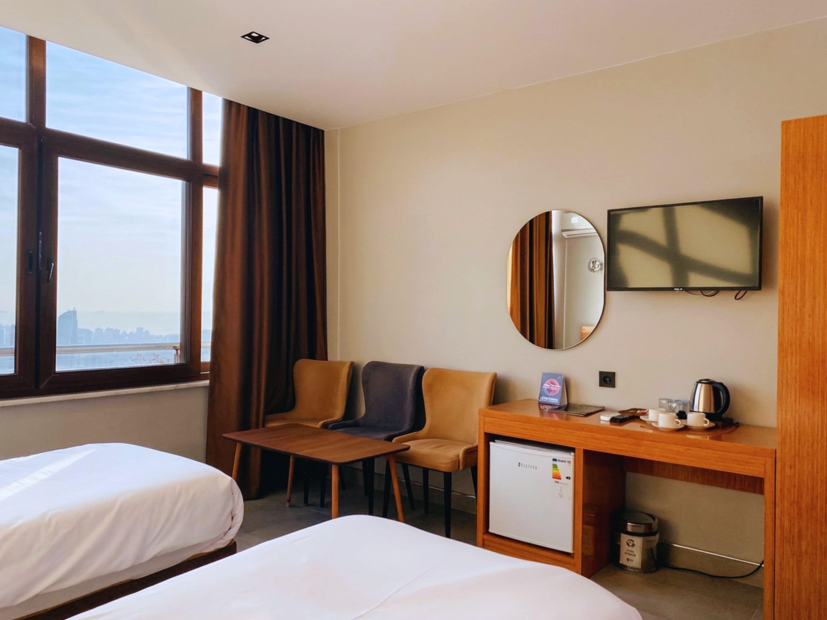 Ein Hotelzimmer mit zwei Betten, einem Schreibtisch mit Kaffeemaschine, einer kleinen Kühlbox und einem Fernseher an der Wand.