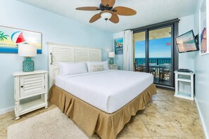 Een slaapkamer met een bed, een plafondventilator, een televisie en een balkon met uitzicht.