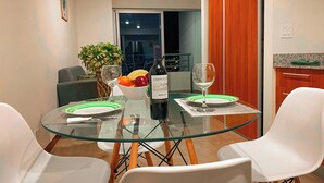 A dining area with a glass table, white chairs, a bowl of fruit, a bottle of wine, and a view of the city at night. - Relaxing Apartment in the heart of San Jose (San José)
