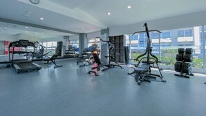 A spacious gym with various exercise equipment, large windows, and a visible clock on the wall. - Relaxing Apartment in the heart of San Jose (San José)