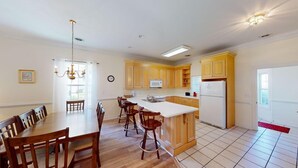 A spacious kitchen with wooden cabinets, a white refrigerator, and a dining area with a wooden table and chairs. - Four Bedroom, 3 Baths, Avian Forest, Scenic View (Pawleys Island)