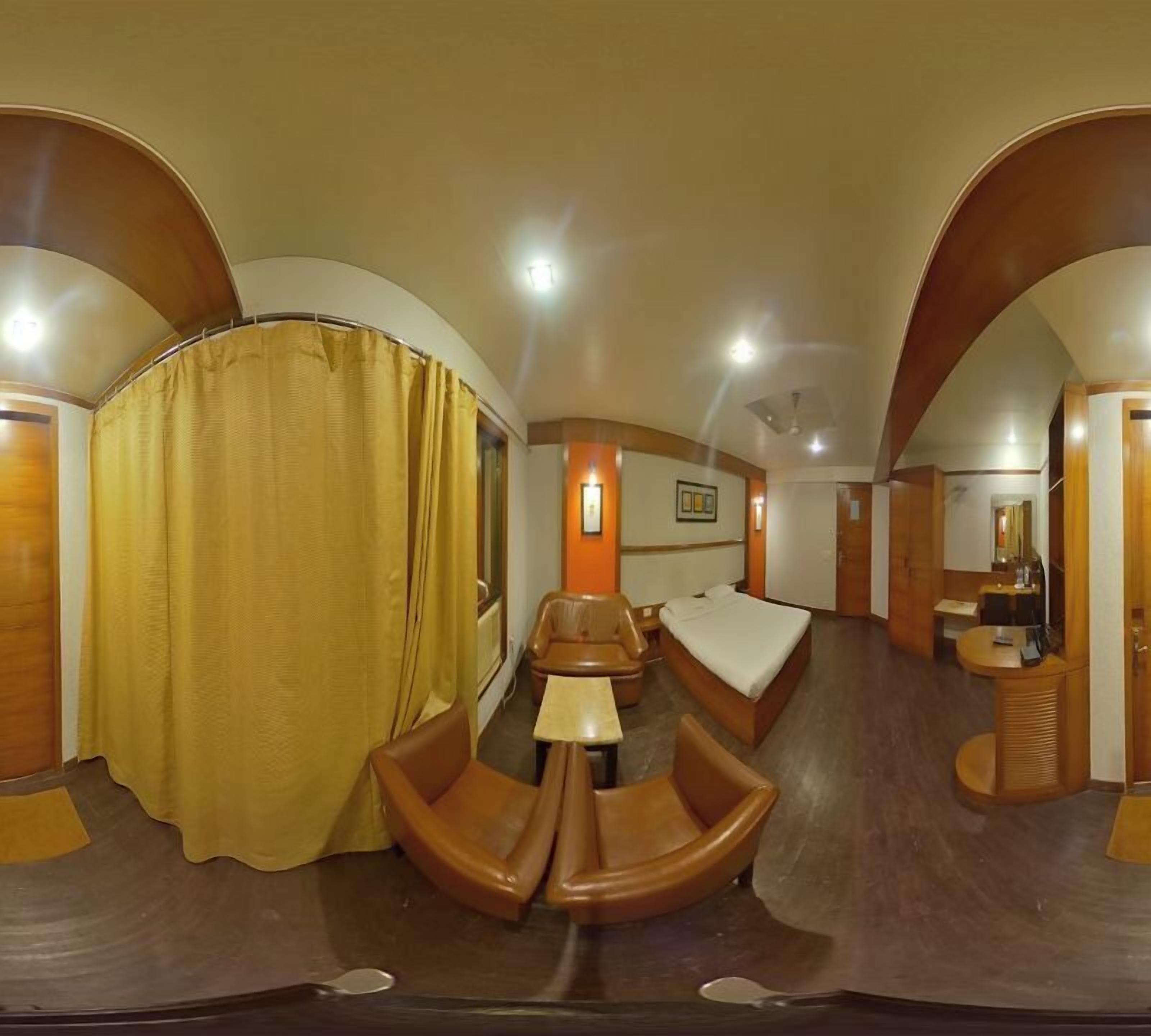 A hotel room with a curved ceiling, a bed, a desk, a chair, and a small table.
