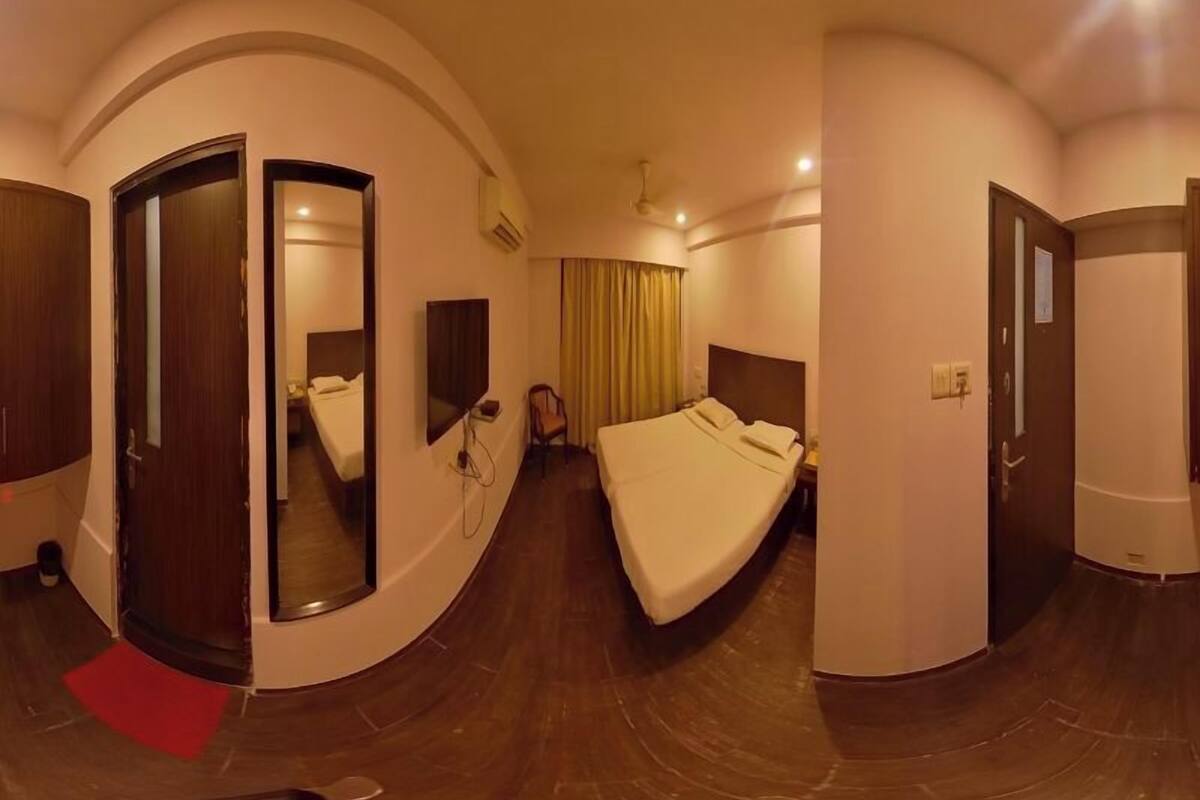 A hotel room with a curved layout, a bed, a desk, a chair, a mirror, and a door.