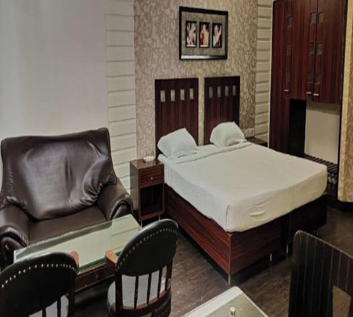 A hotel room with a bed, a leather sofa, a wooden nightstand, a chair, and a mirror.