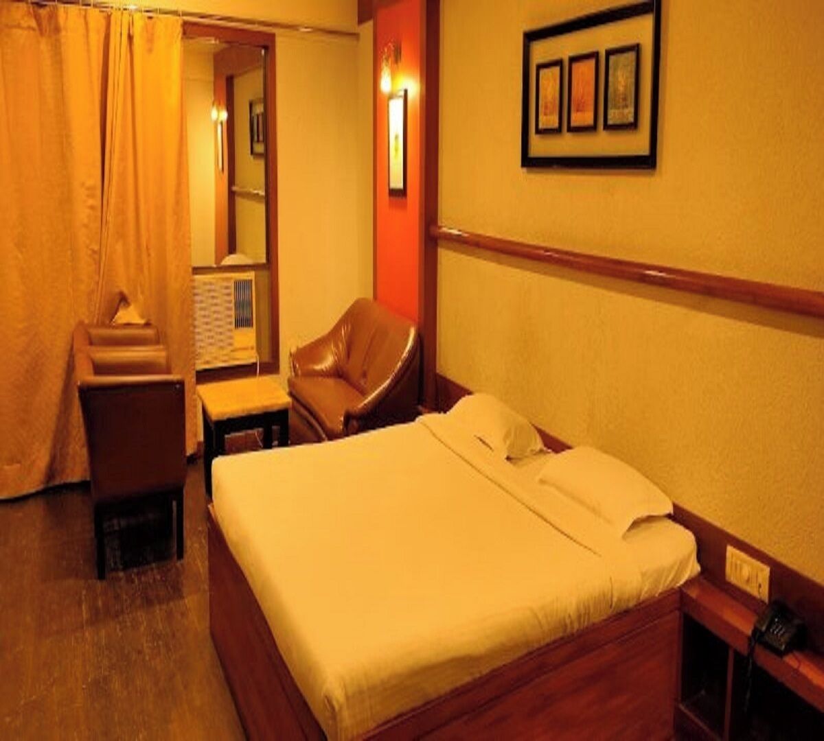 A hotel room with a bed, a chair, a bedside table, a lamp, and a telephone.