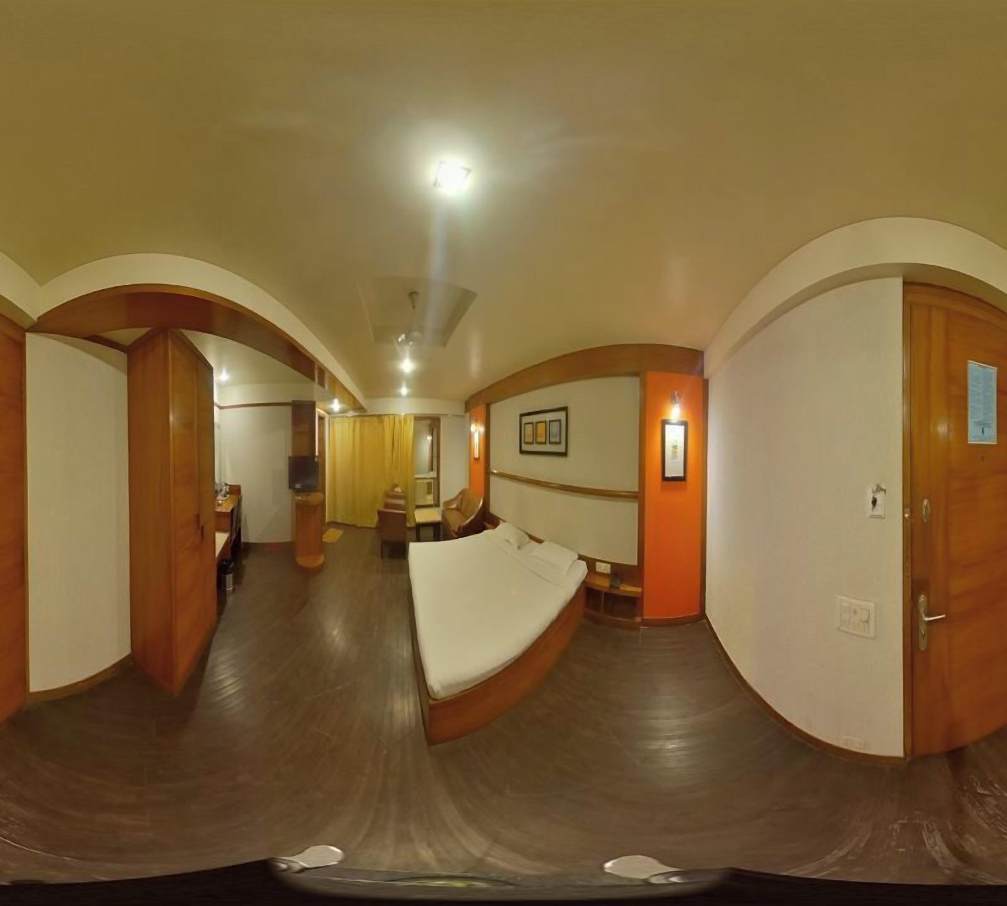 A hotel room with a curved ceiling, wooden flooring, a bed, a desk, and a chair.