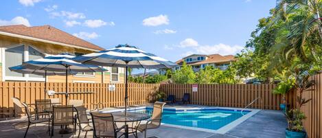 A backyard with a swimming pool, patio furniture, and umbrellas.