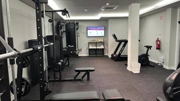 Un gimnasio con equipamiento para levantamiento de pesas, cintas de correr y una banca.