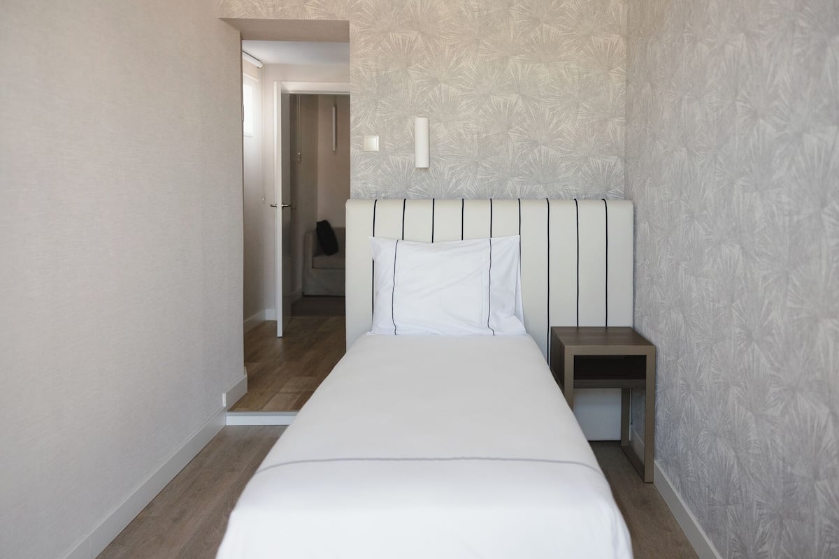 Een slaapkamer met een bed, een nachtkastje, een deur naar een andere kamer en een behang met een patroon.