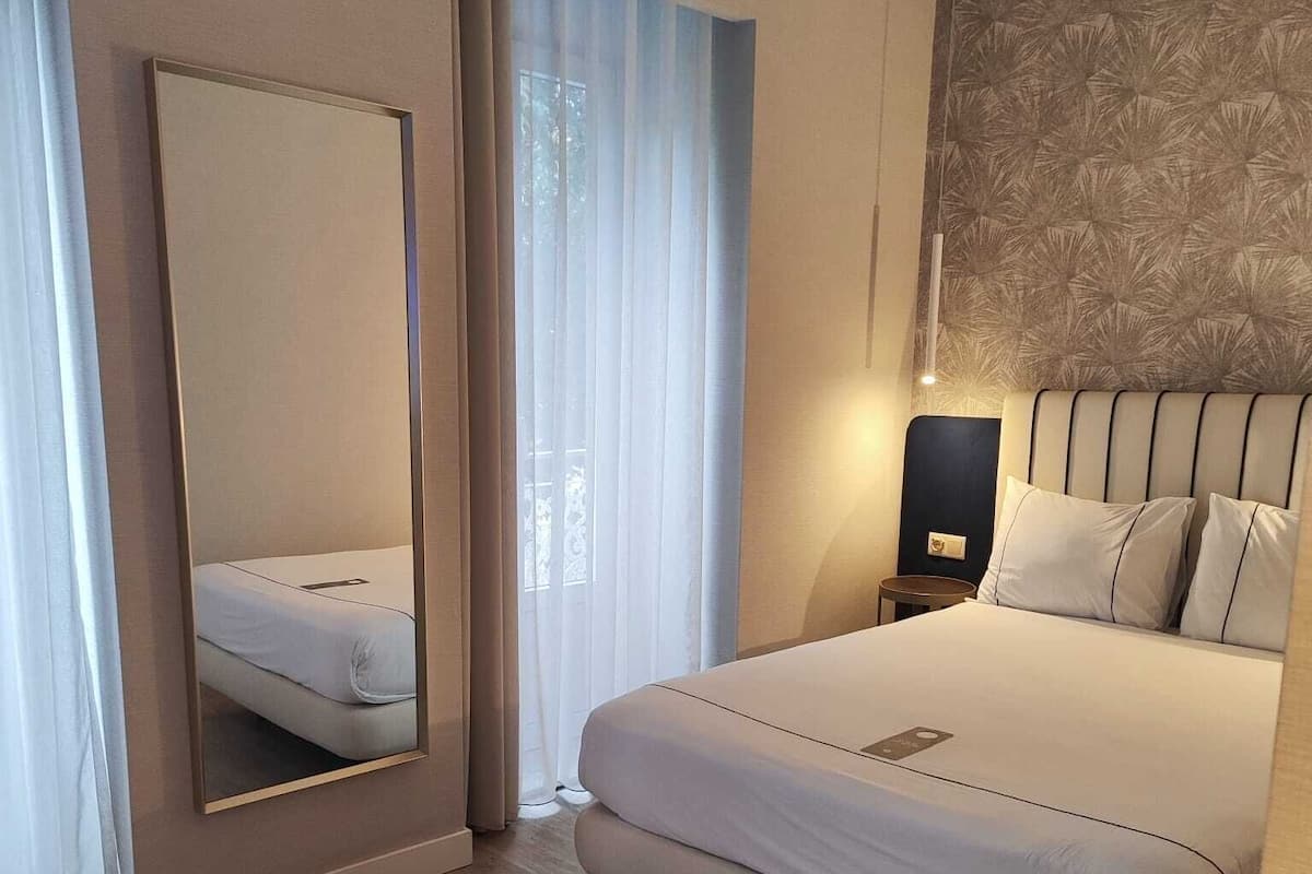 Een moderne hotelkamer met een groot bed, nachtkastje, spiegel en een behang met patroon.