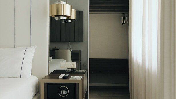 A modern hotel room with a minimalist design, featuring a sofa, a bedside table with a lamp, and a view of the hallway. - M’AR De AR Auria (Lisbon)