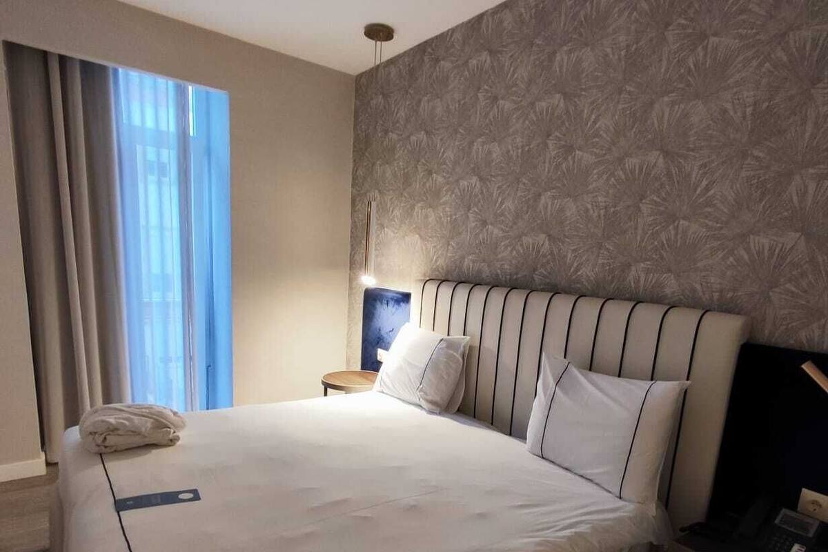 Een moderne hotelkamer met een groot bed, een nachtkastje en een bedtafel.