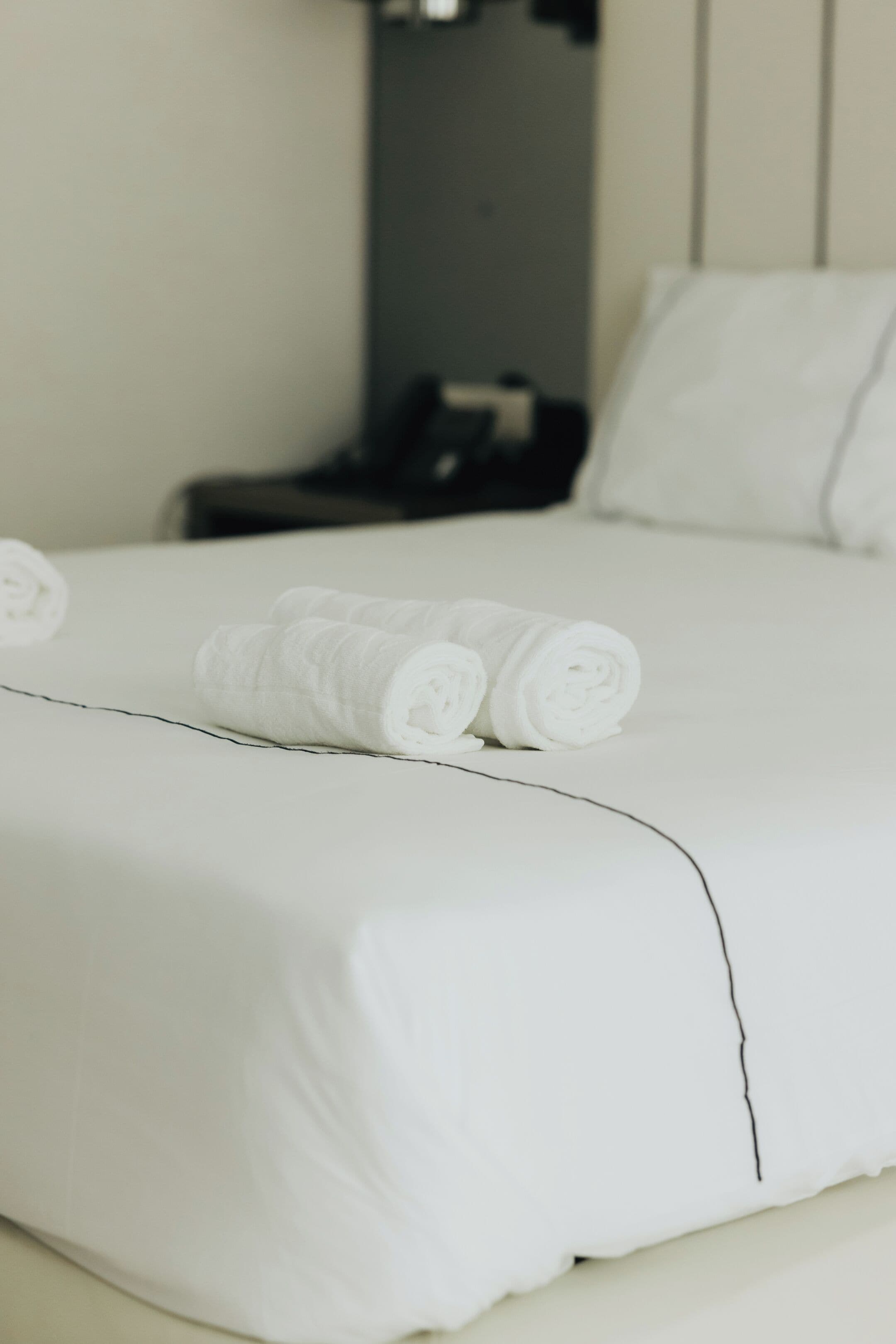 A neatly made bed with white linens and rolled towels.