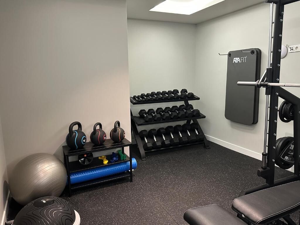 A gym with a squat rack, kettlebells, dumbbells, exercise balls, and a bench.