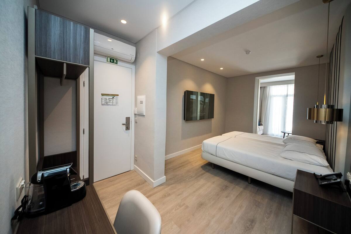Een hotelkamer met een bed, een bureau, een stoel, een koffieapparaat, een kledingkast en een raam.