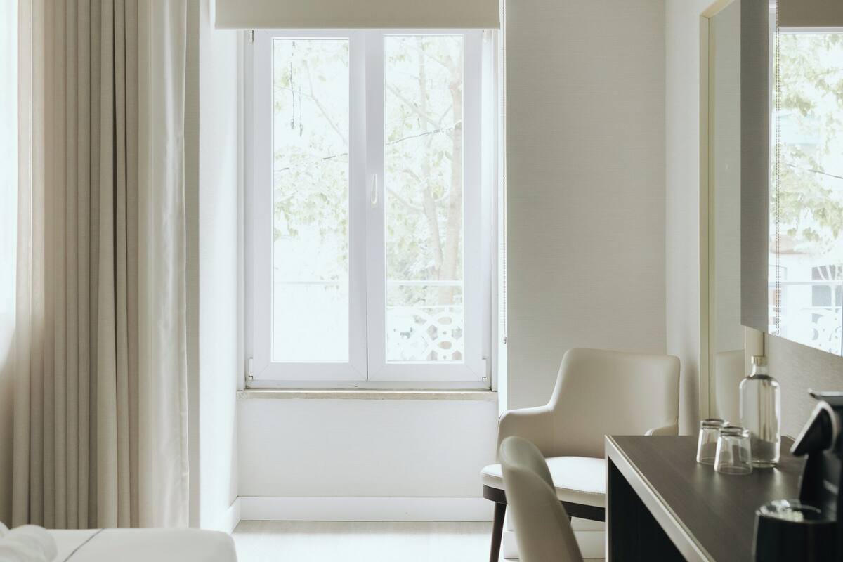 Hotelkamer met een bed, een bureau, een stoel, een groot raam en een spiegel.