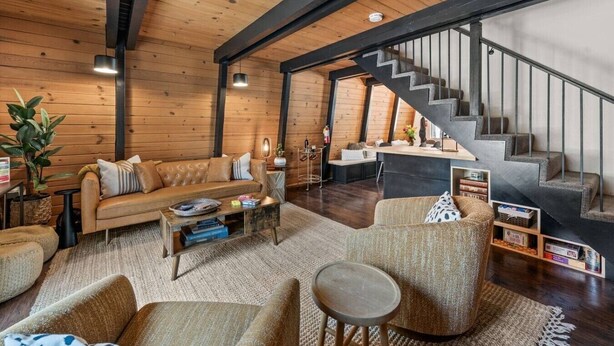 Una sala de estar moderna con techo de madera, un sofá, una mesa de centro y una escalera que sube a un nivel superior.