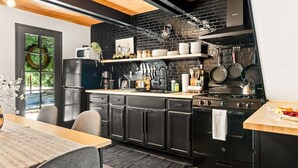 Una cocina moderna con gabinetes negros, techo de madera y salpicadero de ladrillo negro.