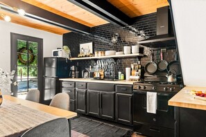 Une cuisine moderne avec des meubles noirs, un plafond en bois et un mur de briques noires derrière le plan de travail.