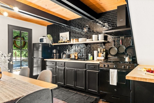 A modern kitchen with black cabinets, a wooden ceiling, and a black brick backsplash.