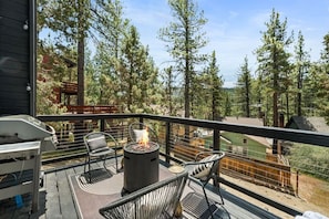A deck with outdoor furniture, a fire pit, and a view of trees and buildings. - 2BR Retreat: EV, Hot Tub, BBQ & Dog-Friendly (Big Bear Lake)