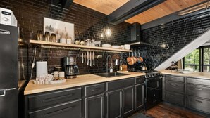 Una cocina con armarios negros, una encimera de madera, una cafetera y utensilios colgados.