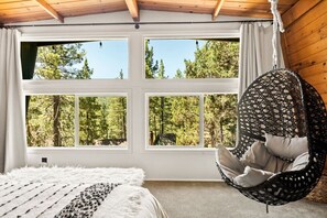 A room with a large window, a hanging chair, and a bed. - 2BR Mid Century Retreat • EV, Hot Tub (Big Bear Lake)