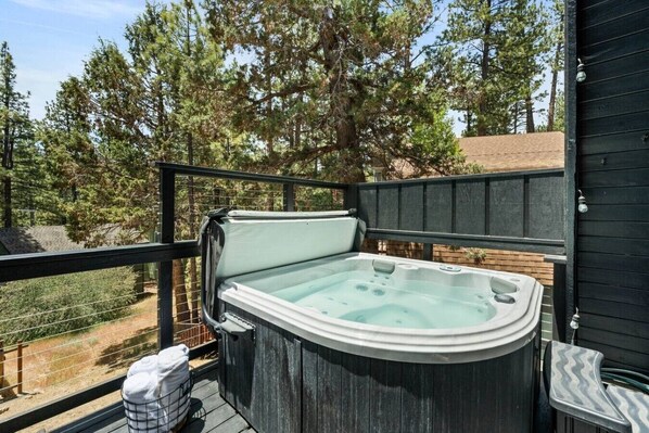 Un jacuzzi en una terraza exterior con barandilla de madera, rodeado de árboles.