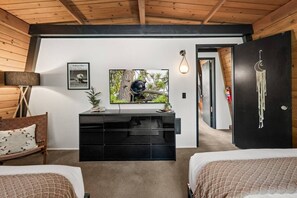 Una habitación con cama, escritorio con computadora, televisor montado en la pared y puerta decorada con un atrapasueños.
