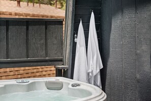 Un jacuzzi con terraza de madera y una puerta negra con toallas blancas colgadas.