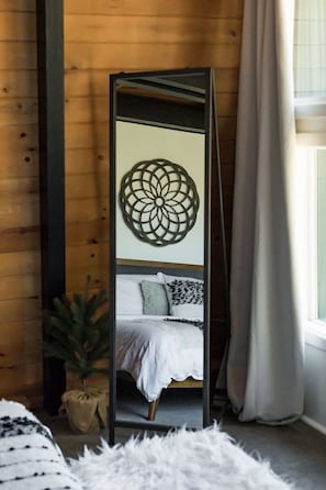 A room with a bed, a decorative wall piece, a potted plant, and a window with curtains. - 2BR Retreat: EV, Hot Tub, BBQ & Dog-Friendly (Big Bear Lake)
