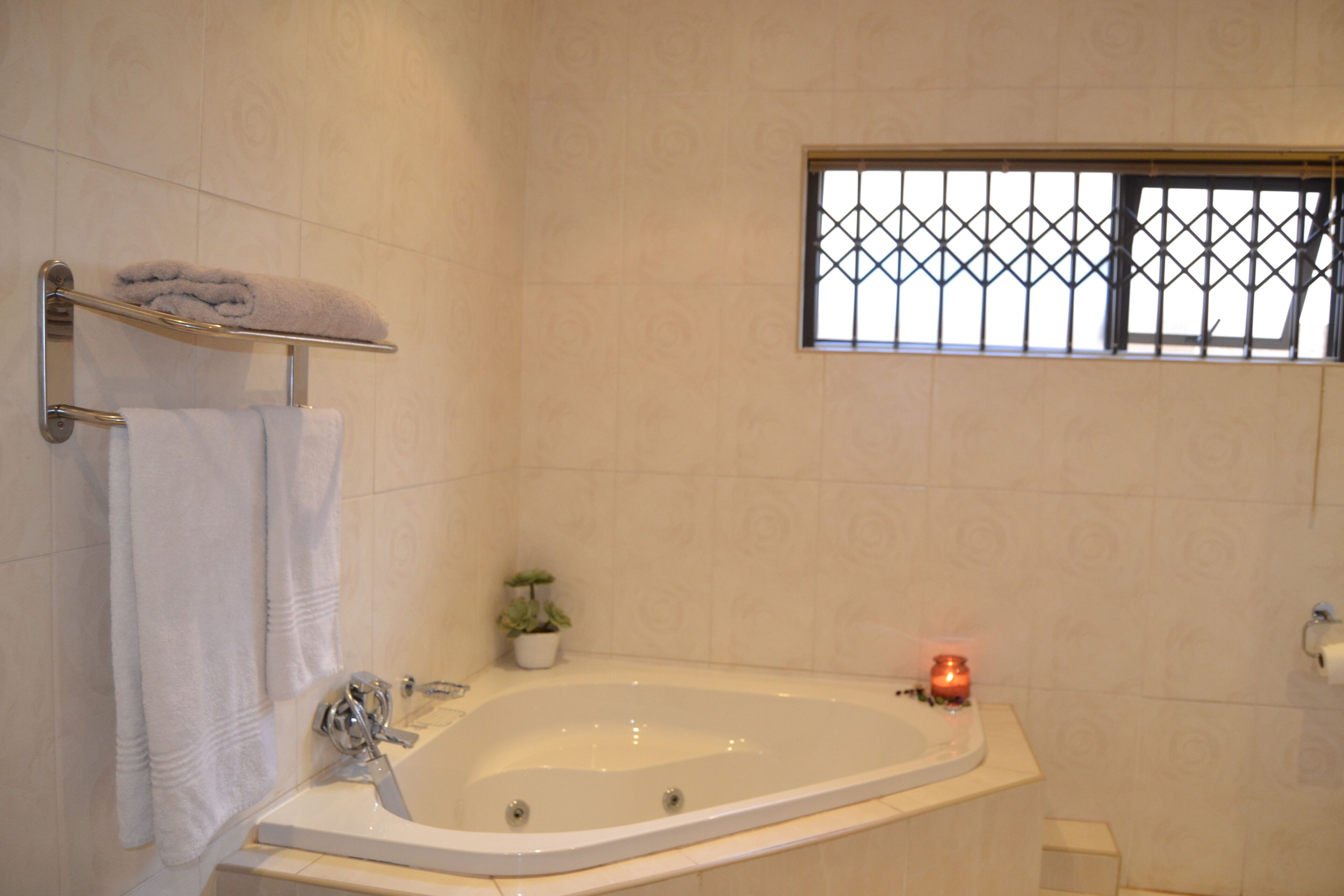 A bathroom with a bathtub, a towel rack, a small potted plant, and a window with bars.