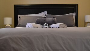 A neatly made bed with a dark headboard, two bedside lamps, and a wall-mounted light fixture. - Hush Guest House (Thabazimbi)