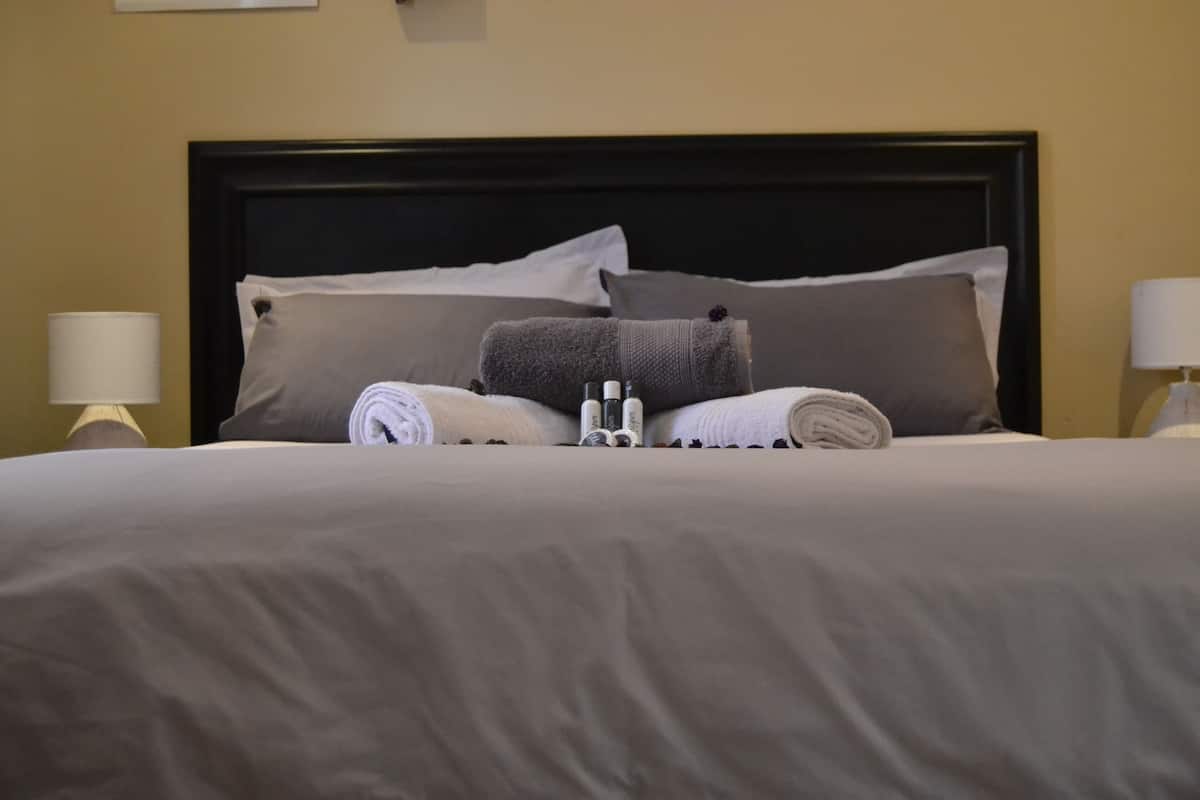 A neatly made bed with a dark headboard, two bedside lamps, and a wall-mounted light fixture.