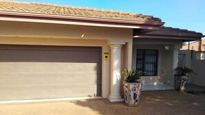 A residential building with a closed garage door, a tiled roof, and a paved driveway. - Hush Guest House (Thabazimbi)