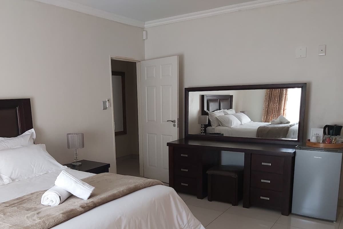 A hotel room with a bed, a dresser, a mirror, a desk, and a coffee maker.